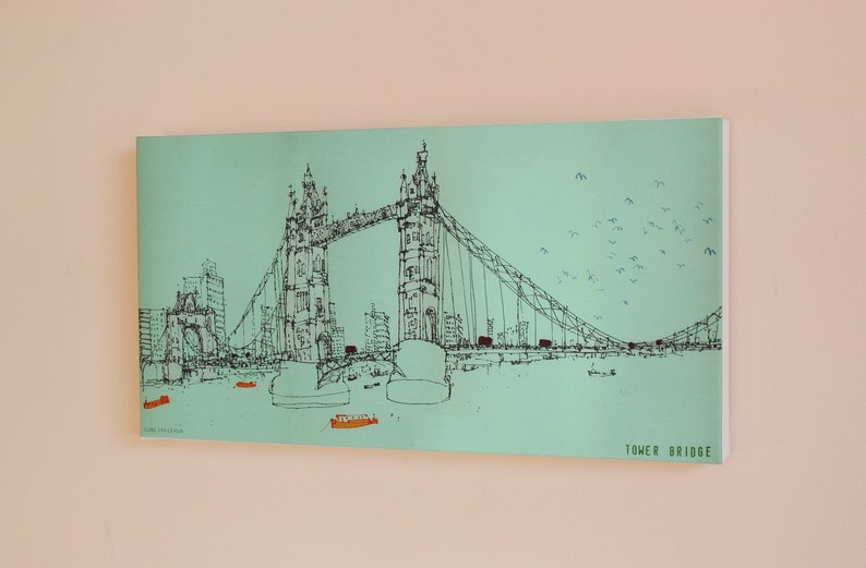 May include: A black and white line drawing of Tower Bridge in London, England. The bridge is depicted against a light blue background with a flock of birds flying overhead. The text "TOWER BRIDGE" is printed in black at the bottom right corner of the image.