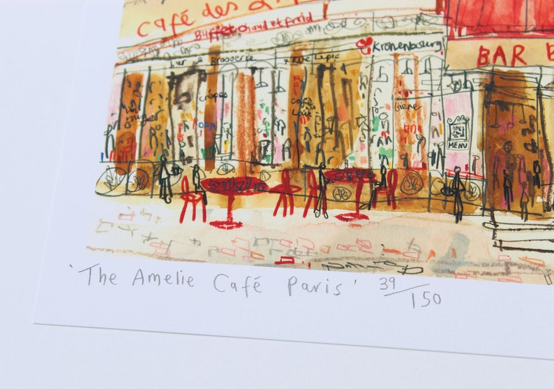 May include: Watercolor print of a Parisian cafe scene, featuring red tables and chairs, and the text "The Amelie Caf&eacute; Paris". The artwork depicts a bustling street scene with storefronts and figures.
