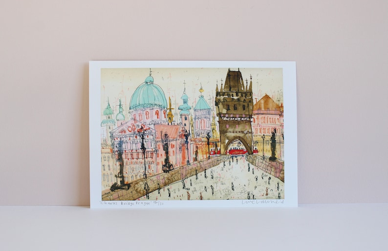 May include: A watercolor painting of the Charles Bridge in Prague, Czech Republic. The painting features the iconic bridge towers, the Vltava River, and the city skyline in the background. The painting is signed "Loraine Levene" in the bottom right corner.