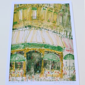 May include: Watercolor print of a Parisian cafe, "Les Deux Magots," with green awnings and umbrellas. The artwork features a detailed depiction of the building's facade, outdoor seating, and the cafe's name in cursive.