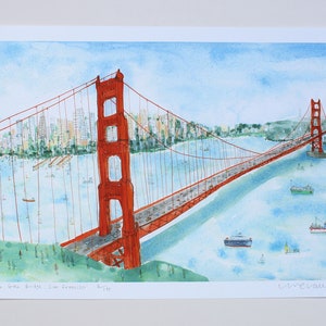 May include: A watercolor print depicting the Golden Gate Bridge in San Francisco, featuring the iconic orange-red bridge spanning blue water with boats, a city skyline in the background, and the handwritten text 'The Golden Gate Bridge, San Francisco'.