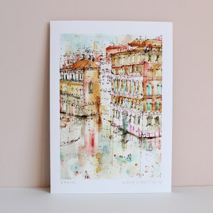 May include: Watercolour painting of buildings in Venice, Italy. The buildings are painted in shades of yellow, orange, and red. The water in the canal is a light blue colour. The painting is signed "Venice" in the bottom left corner and "Love Venice" in the bottom right corner.