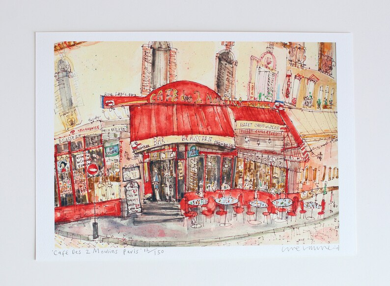May include: Watercolor print of a Parisian cafe, "Cafe des 2 Moulins", with a red awning and outdoor seating. The artwork features detailed architectural elements and street scenes, capturing the essence of a French bistro.