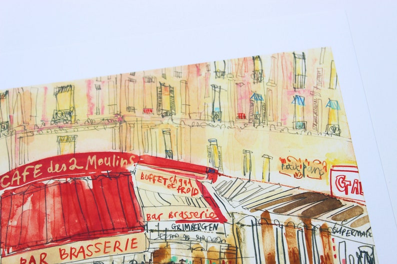 May include: Watercolor painting of a Parisian street scene featuring a cafe with a red awning and the text "CAFE des 2 Moulins". The artwork depicts buildings with detailed architectural elements and various signs.