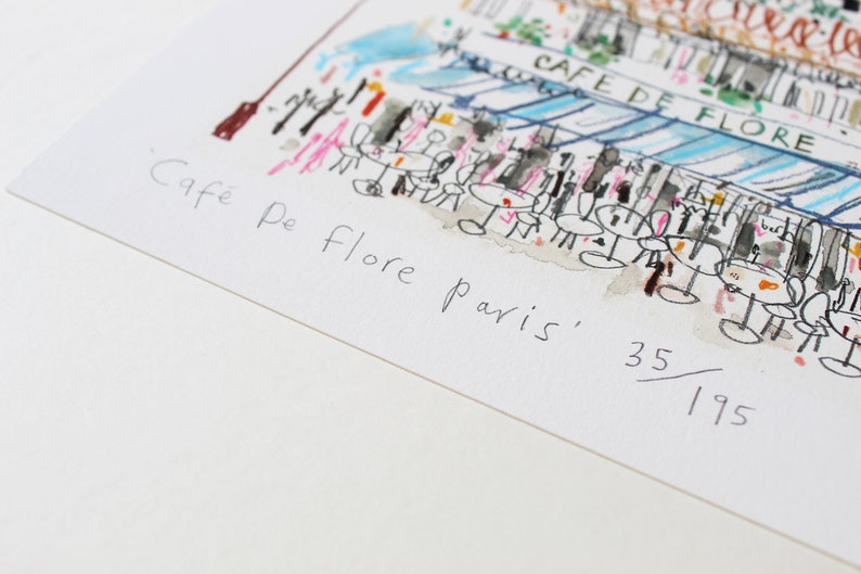 May include: A black and white sketch of a cafe in Paris, France. The cafe is called "Cafe De Flore" and the sketch is numbered 35/195.