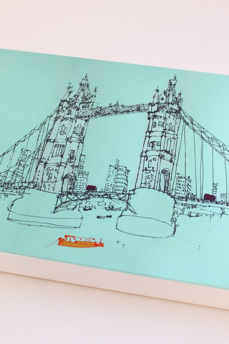 May include: A black and white line drawing of the Tower Bridge in London, England. The bridge is drawn in a simple, minimalist style, with the two towers and the suspension bridge clearly visible. There are small boats in the water below the bridge.
