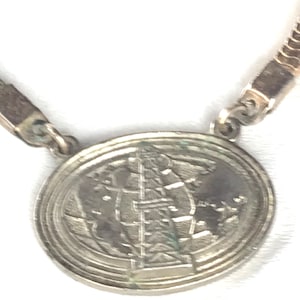 May include: Silver necklace with a round pendant featuring a globe design with a tower in the center.