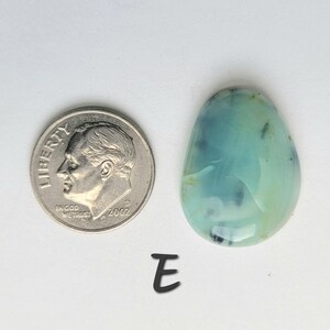 May include: A light blue and green cabochon gemstone with black flecks, measuring approximately the size of a US dime.