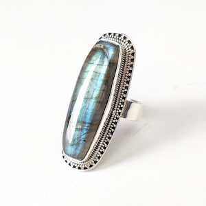 May include: A silver ring with a large, rectangular, iridescent labradorite gemstone set in a silver bezel with a decorative border.