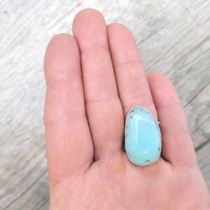 May include: A silver ring with a light blue oval-shaped gemstone. The gemstone has a slightly cloudy appearance.