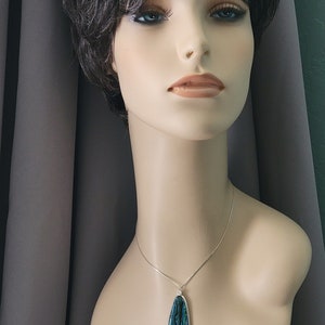 May include: A pendant necklace featuring a teardrop-shaped pendant with a silver-colored border. The pendant has a blue and green iridescent pattern. The necklace is displayed on a mannequin.