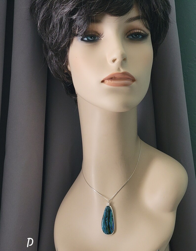 May include: A pendant necklace featuring a teardrop-shaped pendant with a silver-colored border. The pendant has a blue and green iridescent pattern. The necklace is displayed on a mannequin.