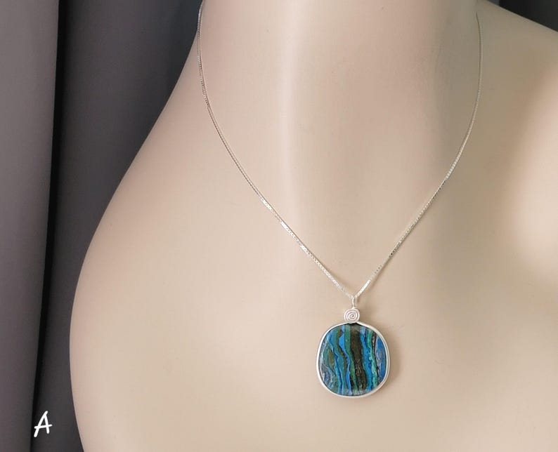 May include: A silver necklace with a square pendant. The pendant features a blue, green, and black marbled design encased in a silver frame. The necklace is displayed on a mannequin.