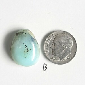 May include: A light blue and green oval-shaped gemstone with black inclusions. The gemstone is about the size of a US dime.