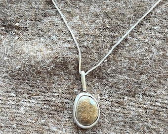 May include: A silver necklace featuring a smooth, rounded pendant with a textured, speckled brown stone center. The pendant is held by a simple silver bail attached to a thin, delicate silver chain, creating a clean and balanced jewelry piece.