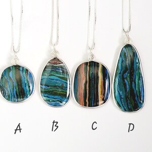 May include: Four silver pendant necklaces with unique, colorful stone pendants. The pendants are various shapes: round, oval, rectangular, and teardrop. Each stone features blue, green, and brown hues. The necklaces are displayed against a white background.