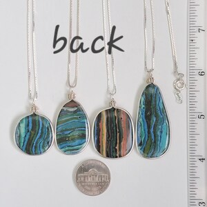 May include: Four silver necklaces with pendant stones in various shapes. The stones feature blue, green, and brown layered patterns. The word "back" is written above the necklaces. A nickel is included for size reference.