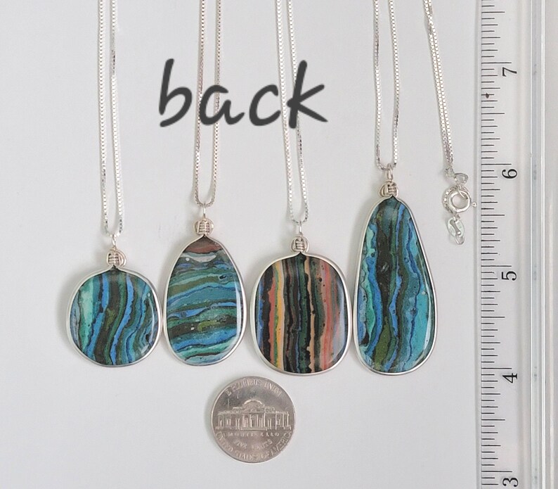 May include: Four silver necklaces with pendant stones in various shapes. The stones feature blue, green, and brown layered patterns. The word "back" is written above the necklaces. A nickel is included for size reference.