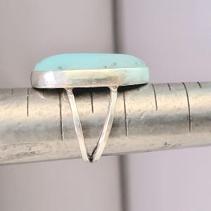 May include: A silver ring with a light blue oval-shaped gemstone. The ring is shown on a ruler, with the gemstone measuring approximately 1 inch in length.