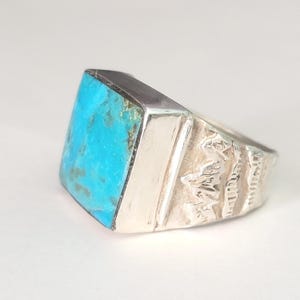 May include: A silver ring with a large, square turquoise stone. The turquoise is a vibrant blue-green color. The ring has a textured design on the side and a polished silver band.