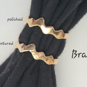 May include: Two gold-colored brass rings with a wavy design. One ring has a polished finish, and the other has a textured, hammered appearance. The word "Brass" is written in black script.