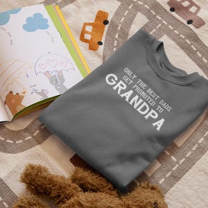 May include: A dark gray sweatshirt with the text "Only the best dads get promoted to Grandpa" in white lettering.