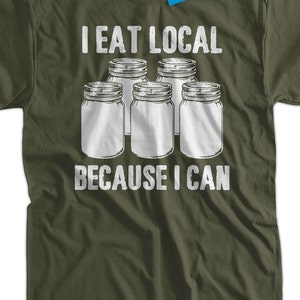 May include: A green t-shirt with white text that reads "I eat local because I can". The text is surrounded by five white mason jars.