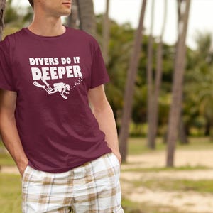 May include: A maroon t-shirt with a white graphic of a scuba diver and the text "Divers Do It Deeper".