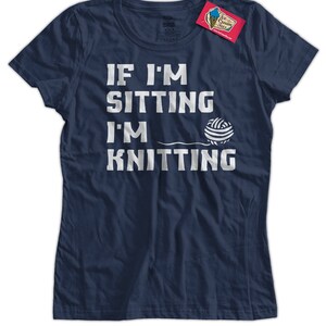 May include: A navy blue t-shirt with the text "If I'm sitting I'm knitting" in white lettering. A white yarn ball is next to the text.