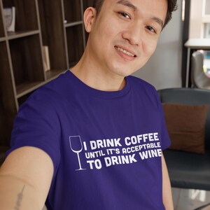 May include: A purple t-shirt with white text that reads "I drink coffee until it's acceptable to drink wine". The text is accompanied by a white outline of a wine glass.