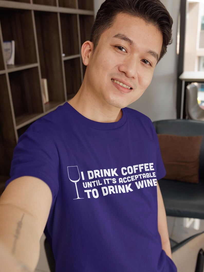 May include: A purple t-shirt with white text that reads "I drink coffee until it's acceptable to drink wine". The text is accompanied by a white outline of a wine glass.