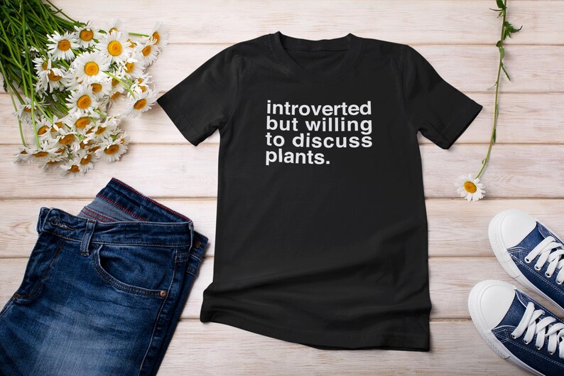 K&ouml;nnte beinhalten: Schwarzes T-Shirt mit wei&szlig;em Text, der "introvertiert, aber bereit, &uuml;ber Pflanzen zu diskutieren" lautet.