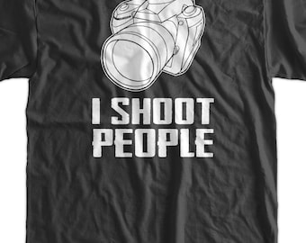 May include: Dark gray t-shirt with a white outline of a camera and the text "I SHOOT PEOPLE" in bold, white letters. A blue tag with text hangs from the collar. A fun gift for photographers.