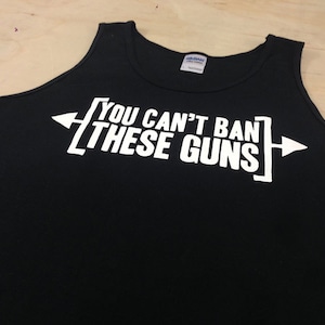 Pu&ograve; includere: Canotta nera con testo bianco che recita "YOU CAN'T BAN THESE GUNS" con frecce su entrambi i lati del testo.