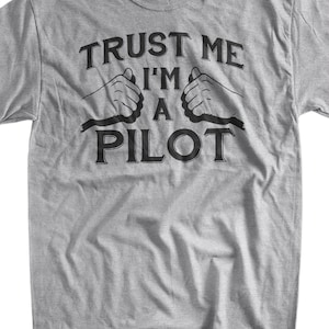 May include: Gray t-shirt with black text that reads "Trust me I'm a pilot" with two black hand gestures making the "I'm a pilot" sign.