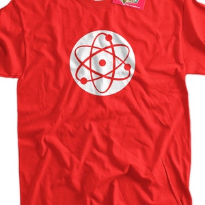 May include: A red t-shirt with a white atom symbol design within a white circle. The tee has a crew neck and short sleeves. A tag from "Ice Cream Tees" is attached to the garment.