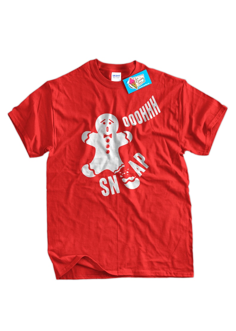 Op de afbeelding: Rood t-shirt met een witte afbeelding van een peperkoeken man die in twee&euml;n breekt, met de witte woorden "OOOOHHH SNAP". Een blauw label met een roze ijslogo is aan het shirt bevestigd.