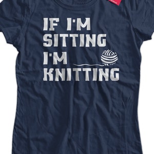 May include: A navy blue t-shirt with white text that reads "If I'm sitting I'm knitting" and a white illustration of a ball of yarn.