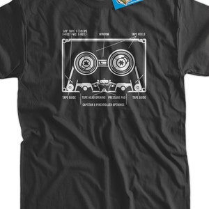 May include: A black t-shirt with a white graphic of a cassette tape. The graphic includes labels for the tape reels, window, tape guide, tape head opening, pressure pad, capstan, and pinchroller openings. The text "1/8" TAPE 1-7/8 IPS (+FAST FWD. & REV.)" is printed above the graphic.