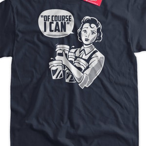 May include: A navy blue t-shirt with a white graphic of a woman holding multiple cups of coffee. The text "Of Course I Can" is in a speech bubble above her head.