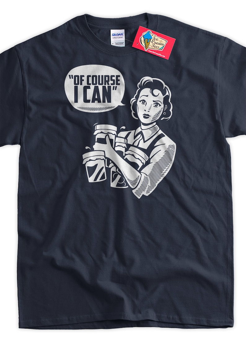 May include: A navy blue t-shirt with a white graphic of a woman holding multiple cups of coffee. The text "Of Course I Can" is in a speech bubble above her head.