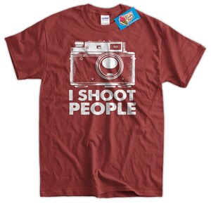 May include: Red t-shirt with a vintage camera graphic and the text "I shoot people".
