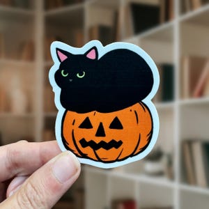 May include: A Halloween-themed sticker featuring a black cat perched atop an orange jack-o'-lantern. The cat has green eyes and pink inner ears. The jack-o'-lantern has a carved face with triangular eyes and a zig-zag mouth. The sticker has a white border.