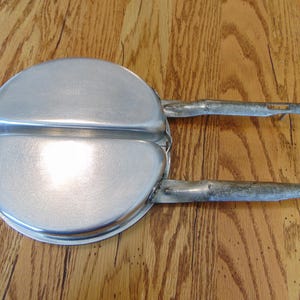 Puede incluir: Una sart&eacute;n de camping vintage de dos piezas, de color plateado, con dos asas. La sart&eacute;n es de metal y tiene una superficie ligeramente desgastada.