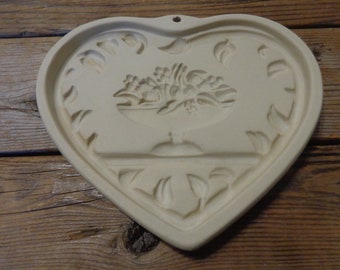 May include: White ceramic heart-shaped cookie cutter with a floral design in the center. The cutter has a hole at the top for hanging.