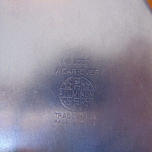 Puede incluir: Un recipiente de metal plateado con el texto "No. 1687 WEAR-EVER ALUMINUM TRADE MARK MADE IN U.S.A." impreso en la parte inferior.