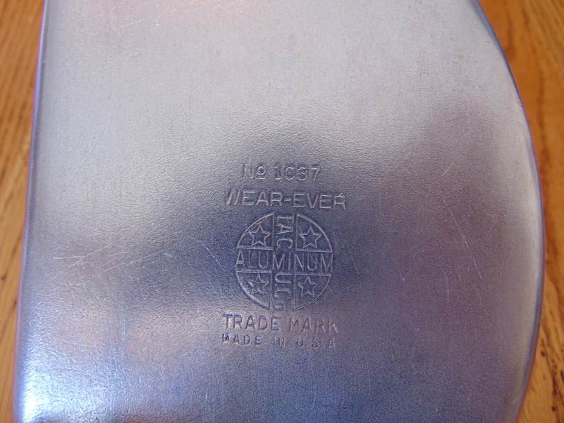 Puede incluir: Un recipiente de metal plateado con el texto "No. 1687 WEAR-EVER ALUMINUM TRADE MARK MADE IN U.S.A." impreso en la parte inferior.