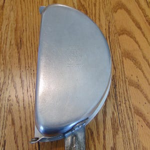 Puede incluir: Un plato de metal plateado en forma de semic&iacute;rculo con un asa. El plato tiene un logotipo que dice "Universal" y "Trade Mark" con "Made in U.S.A." debajo.