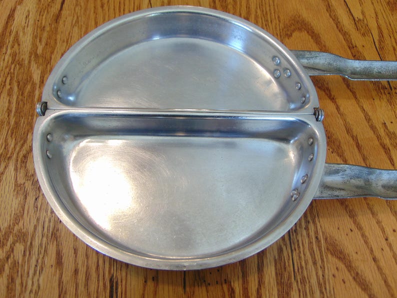 Puede incluir: Un plato de camping dividido de aluminio plateado con un asa con bisagra. El plato est&aacute; dividido en dos secciones y tiene un peque&ntilde;o borde alrededor del borde.