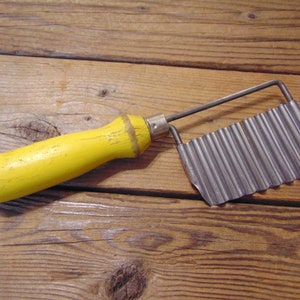 May include: A yellow handled vintage metal potato chipper with a wavy blade.